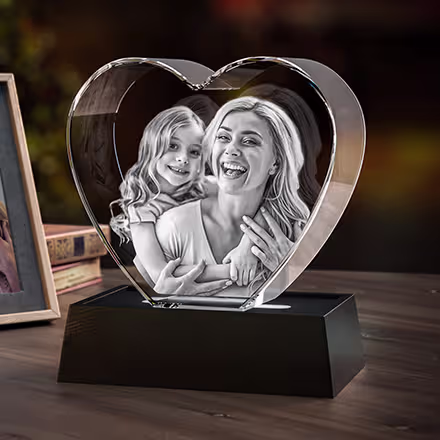 Hjärtformad 3D-fotokristall graverad med ett porträtt av en mamma och dotter, placerad på en svart LED-ljusbas.