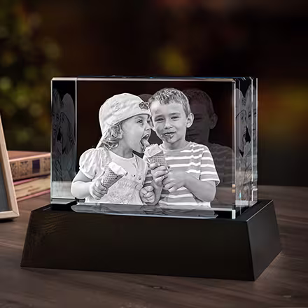 Bred rektangulär 3D-fotokristall graverad med två barn som delar på en glass, placerad på en svart LED-ljusbas bredvid originalfotot.